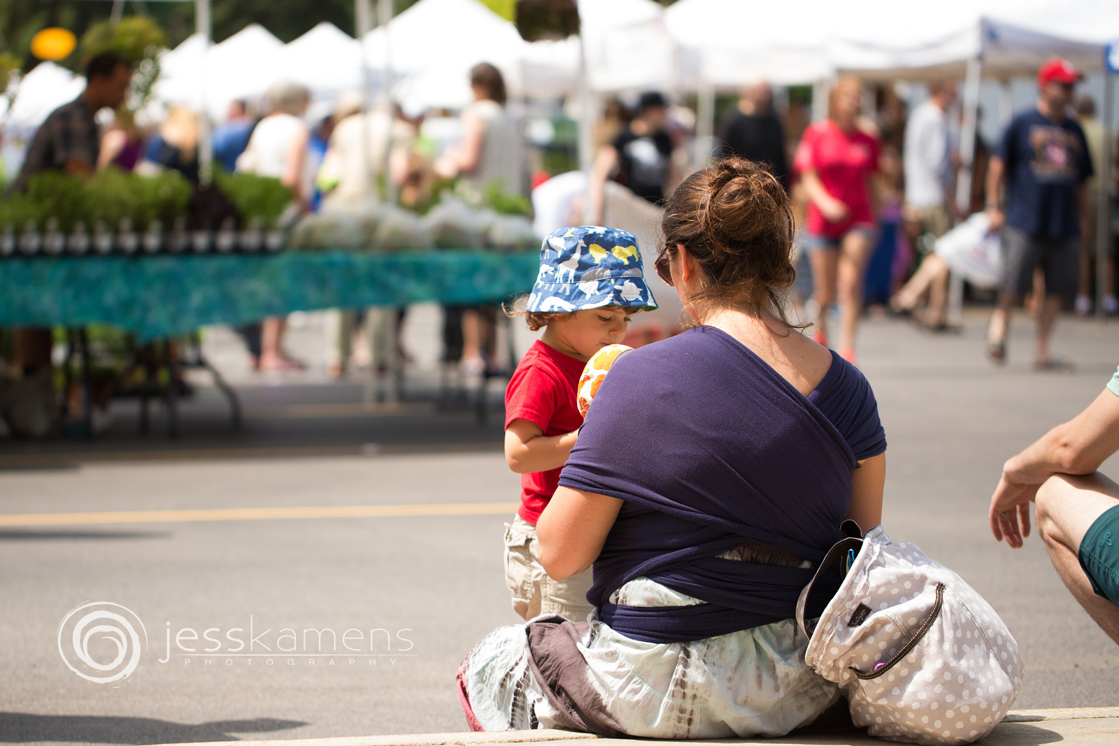 a mother talks to her toddler while babywearing her baby