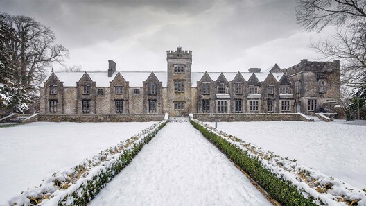 Mallow Castle in Mallow, County Cork, Ireland, photographed in winter with fresh snow covering the formal gardens and historic stone façade under an overcast sky.